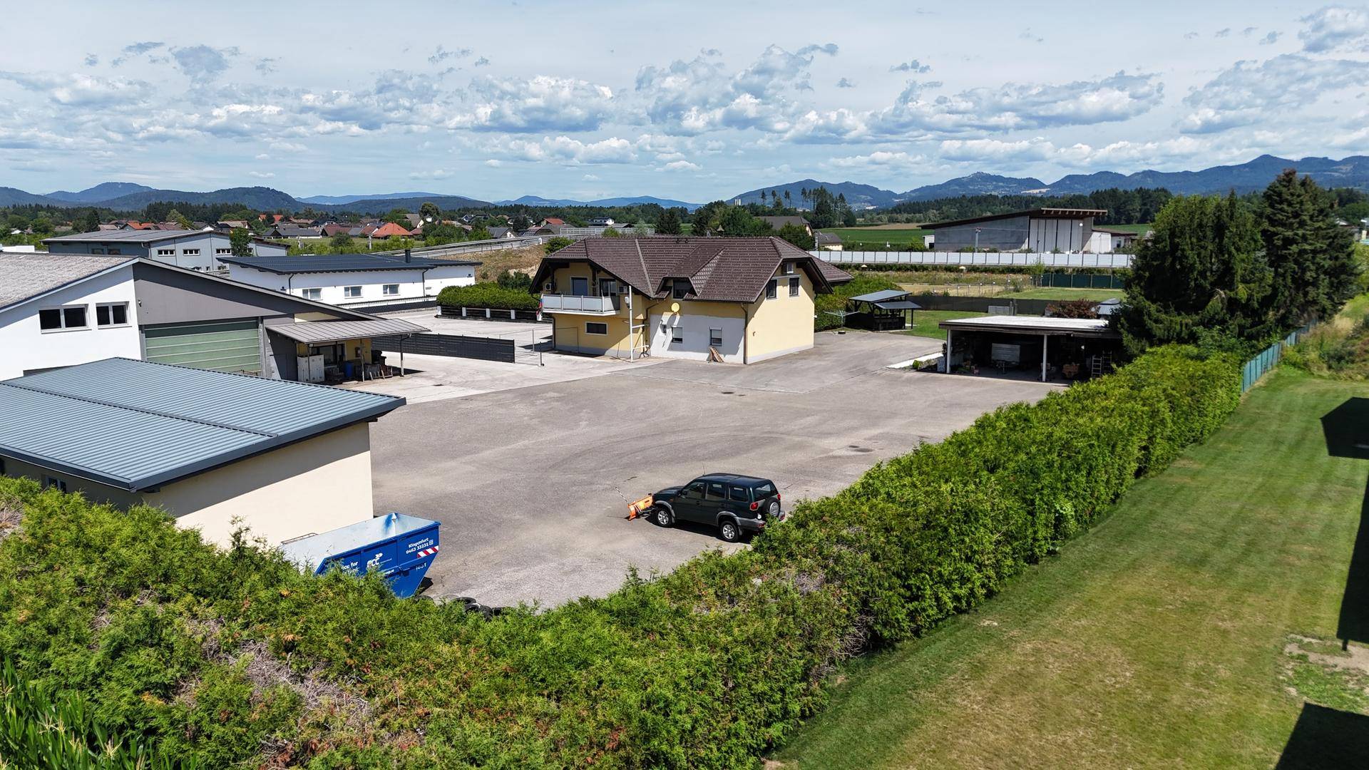 Weitläufige Luftaufnahme eines Gewerbeareals mit Wohnhaus und Blick auf die umliegende Landschaft und Berge.