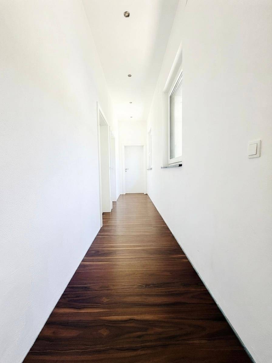 Heller Flur mit modernem Laminatboden und weißen Wänden, der zu weiteren Räumen führt.