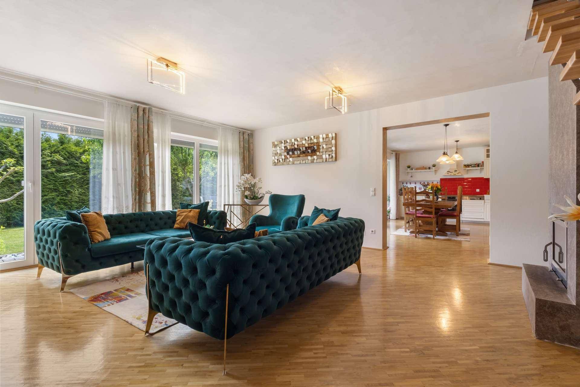 Gemütliches Wohnzimmer mit tealfarbenen Sofas, Parkettboden und Blick in den Garten.