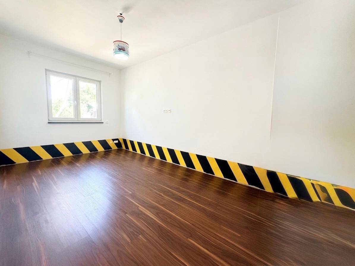 Helles Zimmer mit Holzboden und einer auffälligen gelb-schwarz gestreiften Wanddekoration.