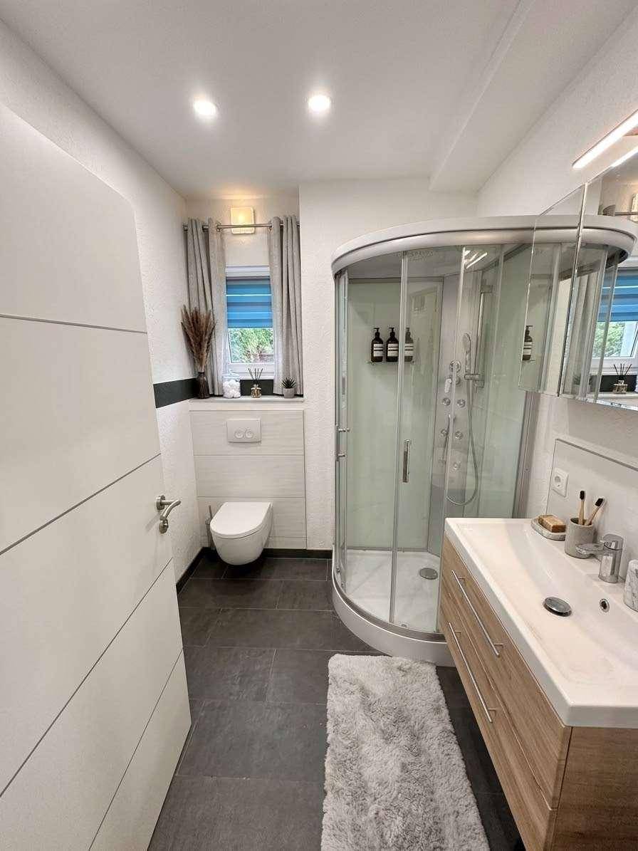 Modernes Badezimmer mit Duschkabine, wandhängendem WC und Holzwaschtisch mit Spiegel.