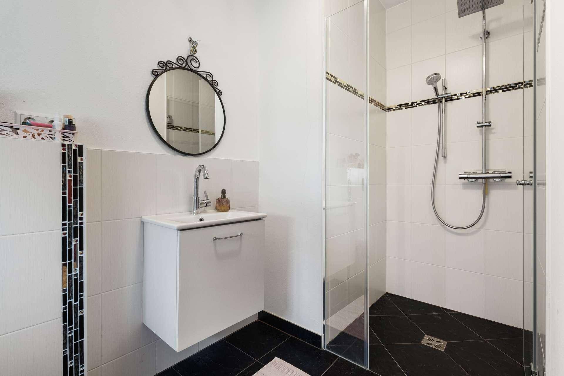 Helles Badezimmer mit moderner Dusche, Waschbecken und dekorativem Spiegel.