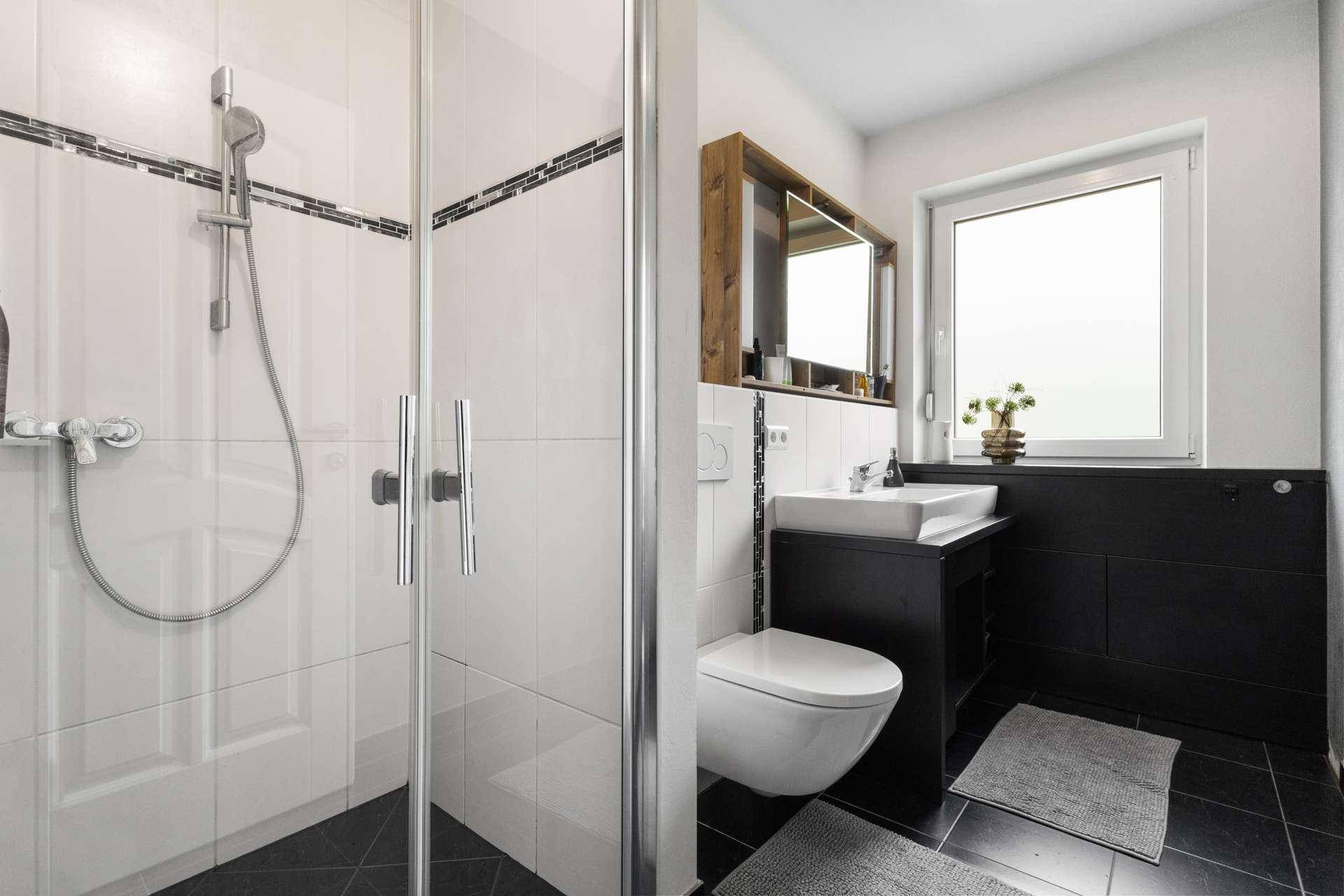 Modernes Badezimmer mit ebenerdiger Dusche, WC, Waschbecken und Fenster für Tageslicht.