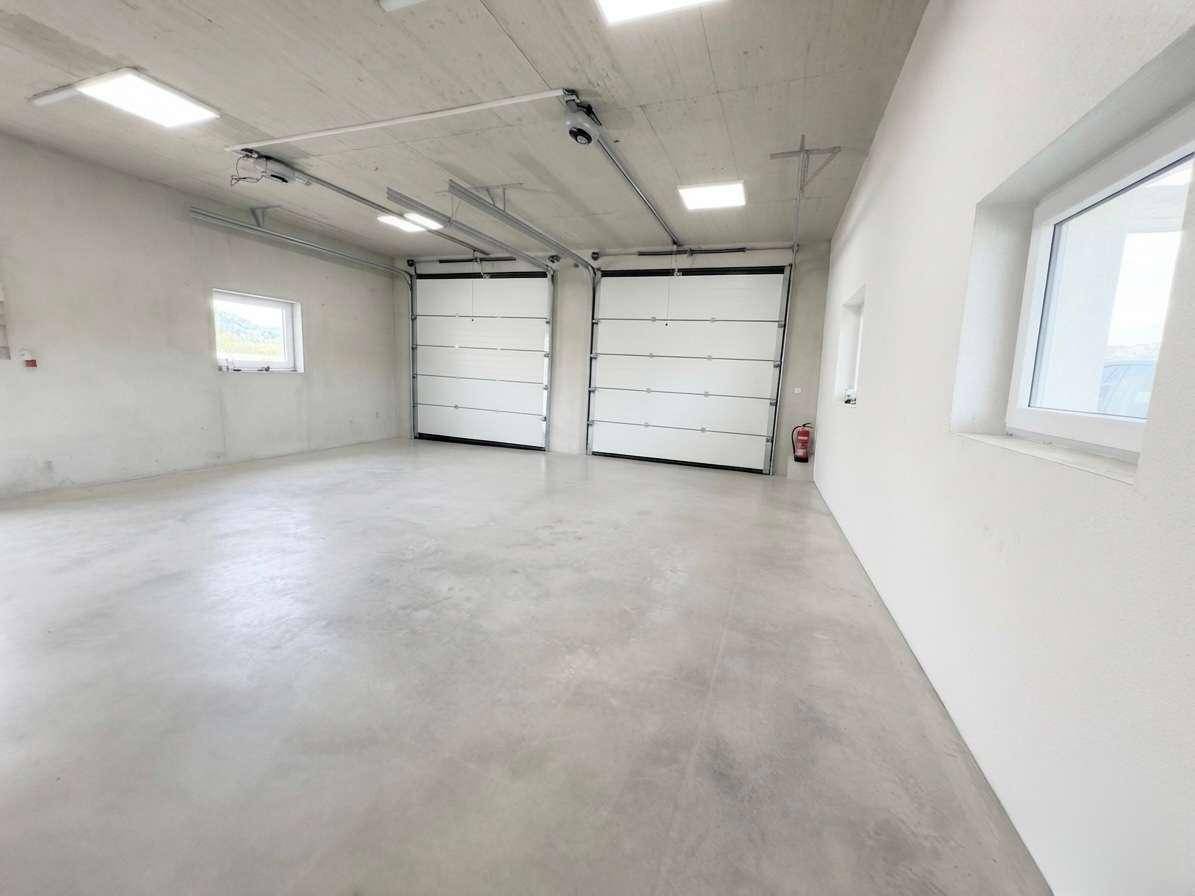 Große Garage mit zwei Rolltoren, Betonboden und Fenstern für ausreichend Tageslicht.