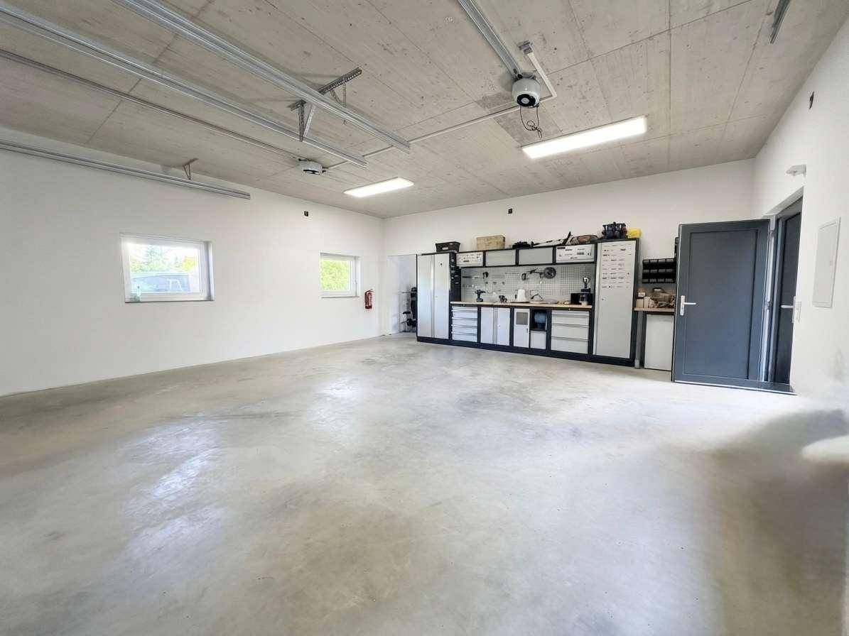 Geräumige Garage mit Betonboden, Werkbankbereich und praktischen Regalen für Lagerung und Arbeit.