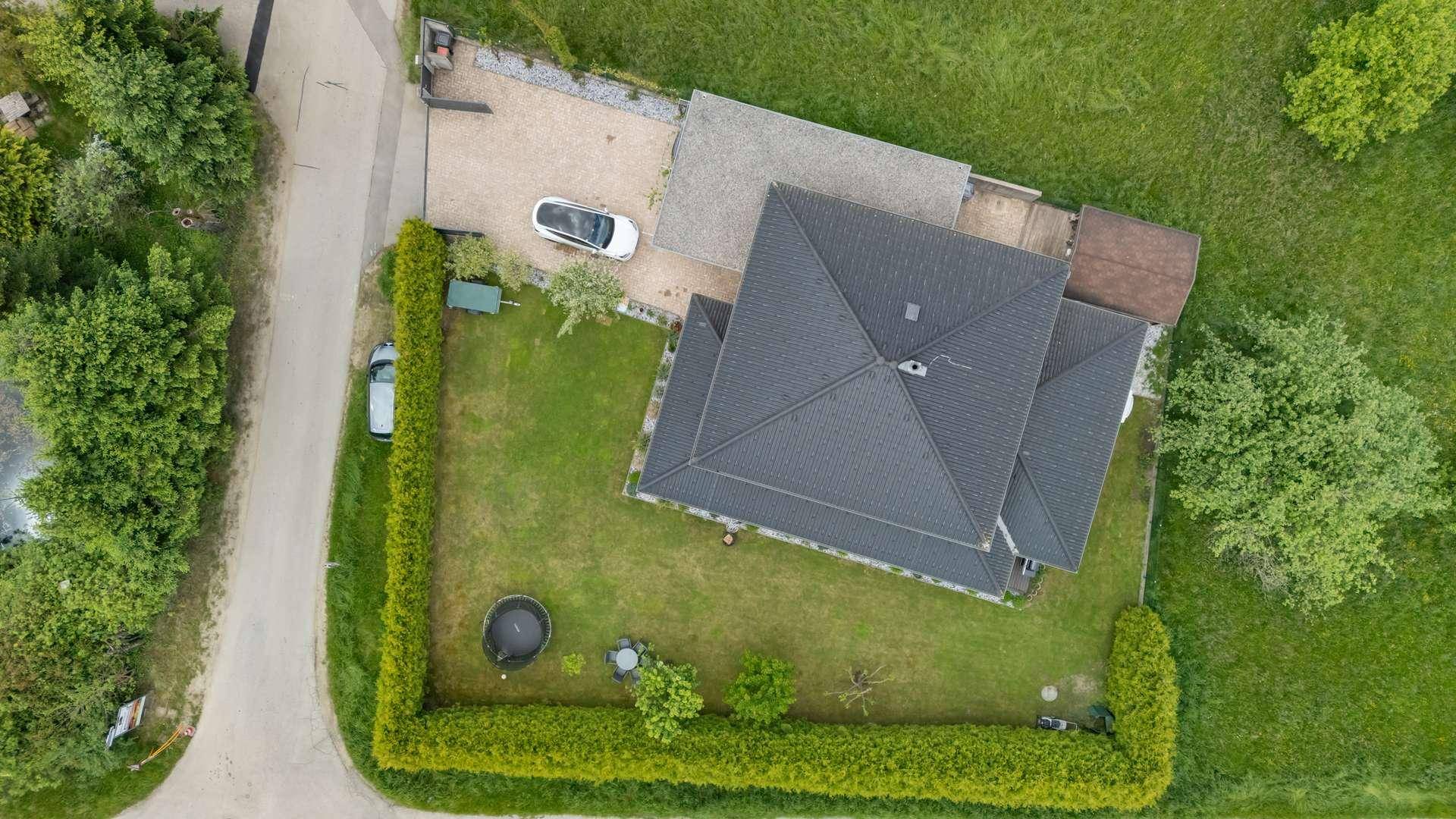 Draufsicht auf das Hausgrundstück mit Garten, Hecke und gepflasterter Zufahrt.