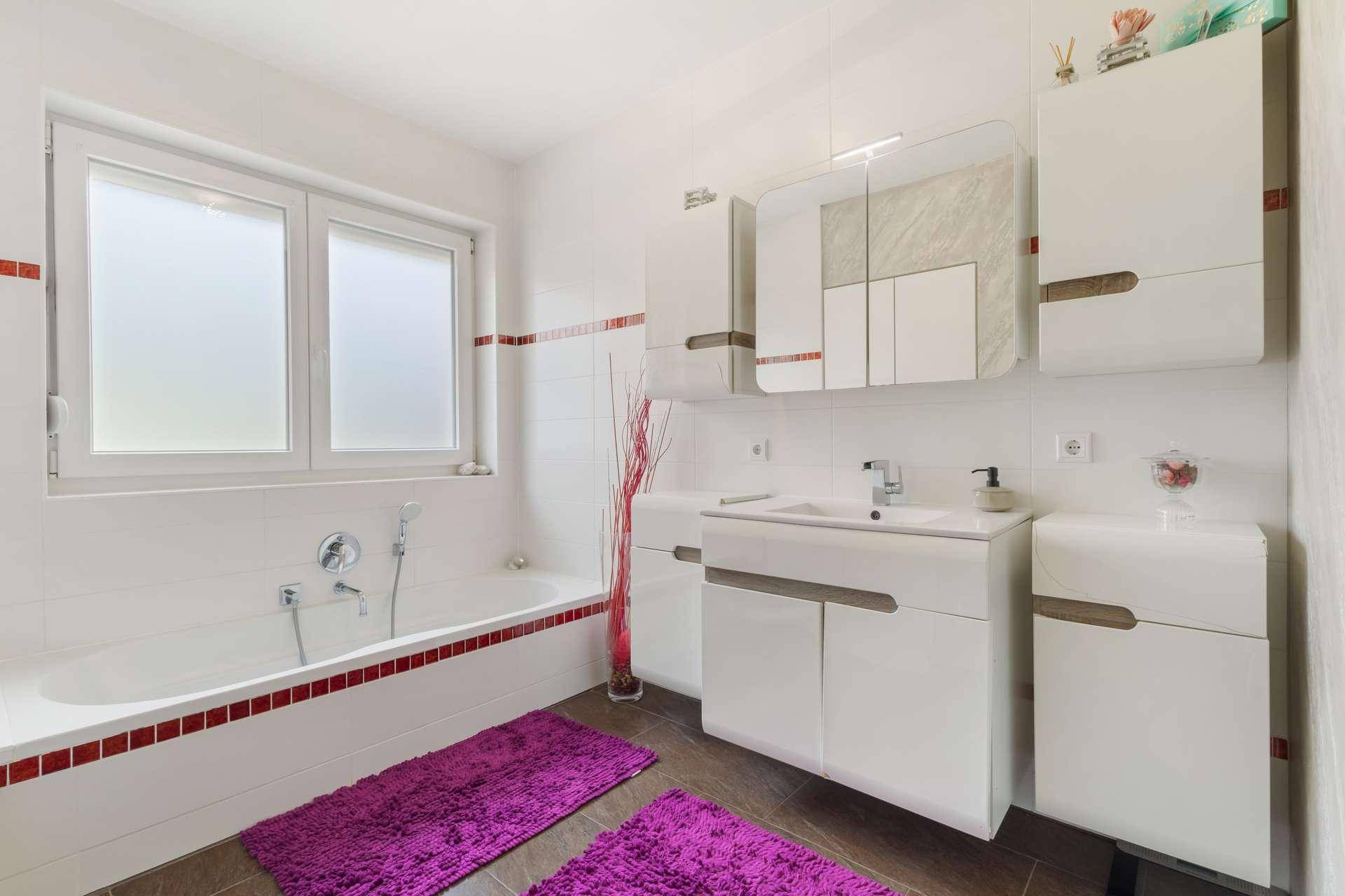 Modernes Badezimmer mit Badewanne, Fenster und weißen Fliesen mit roten Akzenten.