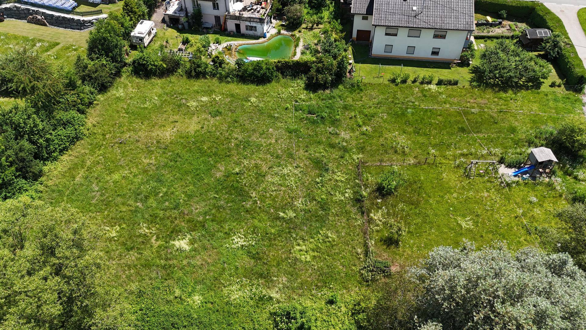 Nahaufnahme eines grünen Grundstücks von oben mit angrenzenden Häusern und Pool.