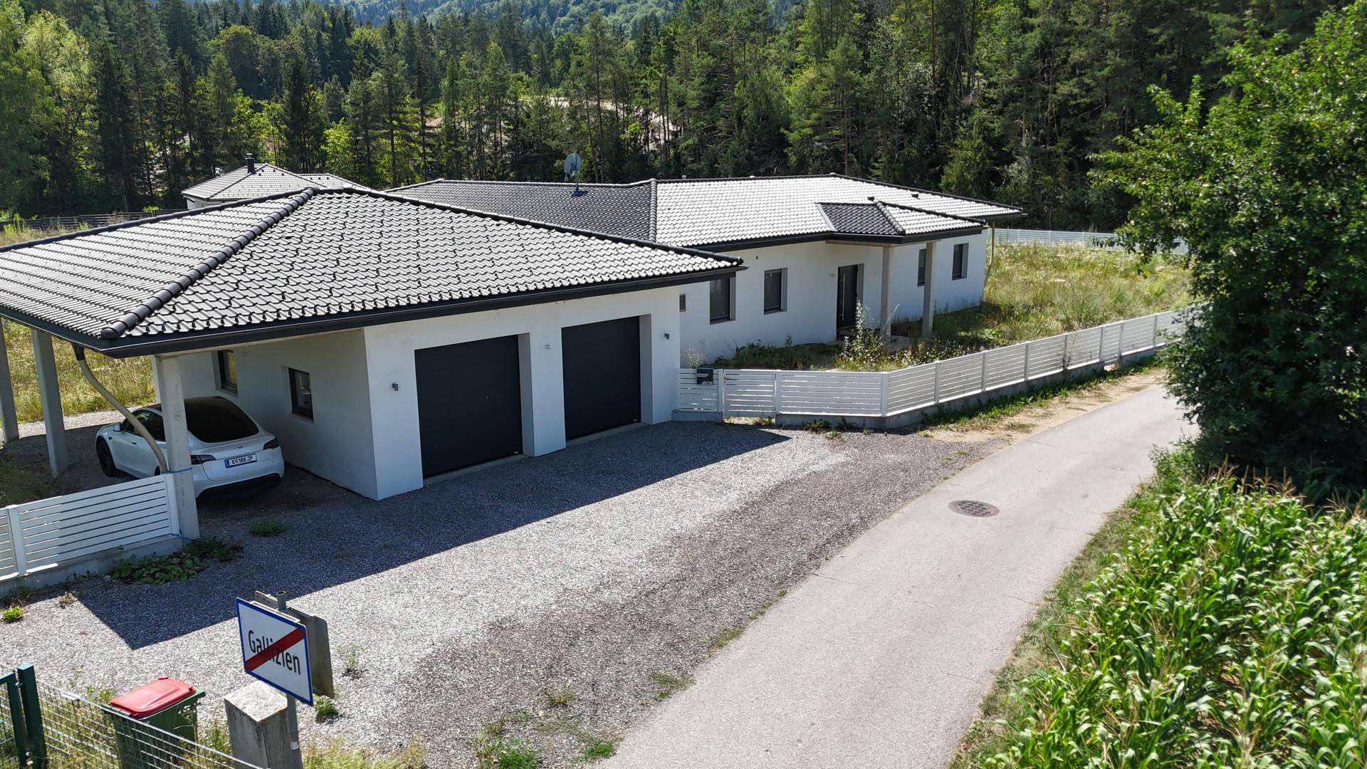 Nahaufnahme des Haupthauses mit Doppelgarage und Carport, umgeben von einer weißen Zaunanlage.