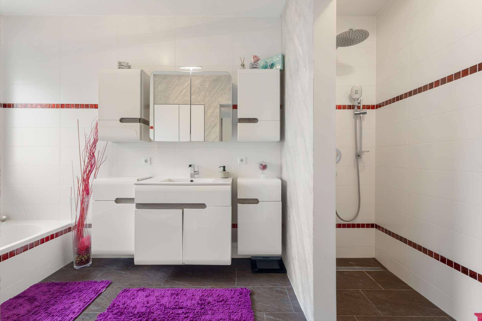 Helles Badezimmer mit begehbarer Dusche, Waschtisch und weißen Fliesen.
