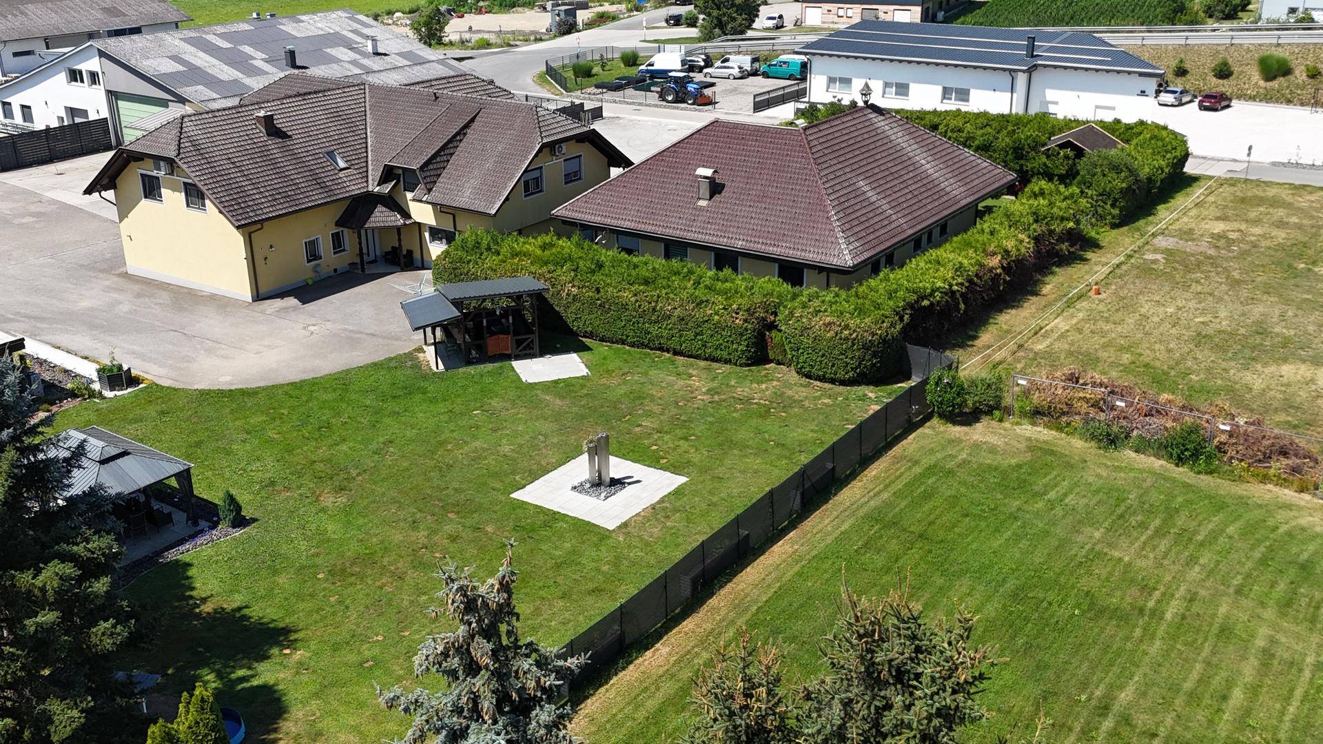 Luftaufnahme eines Anwesens mit zwei Gebäuden, großem Rasenbereich und gepflegter Hecke in ländlicher Umgebung.