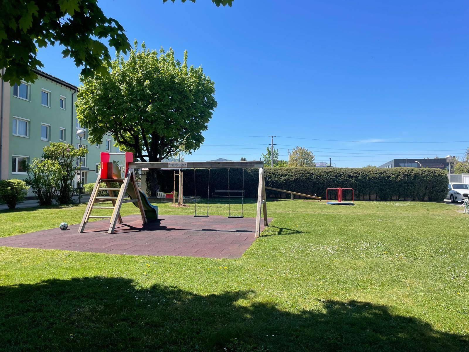 Gemeinschaftlicher Spielplatz mit Schaukeln und Rutsche in grüner Umgebung.