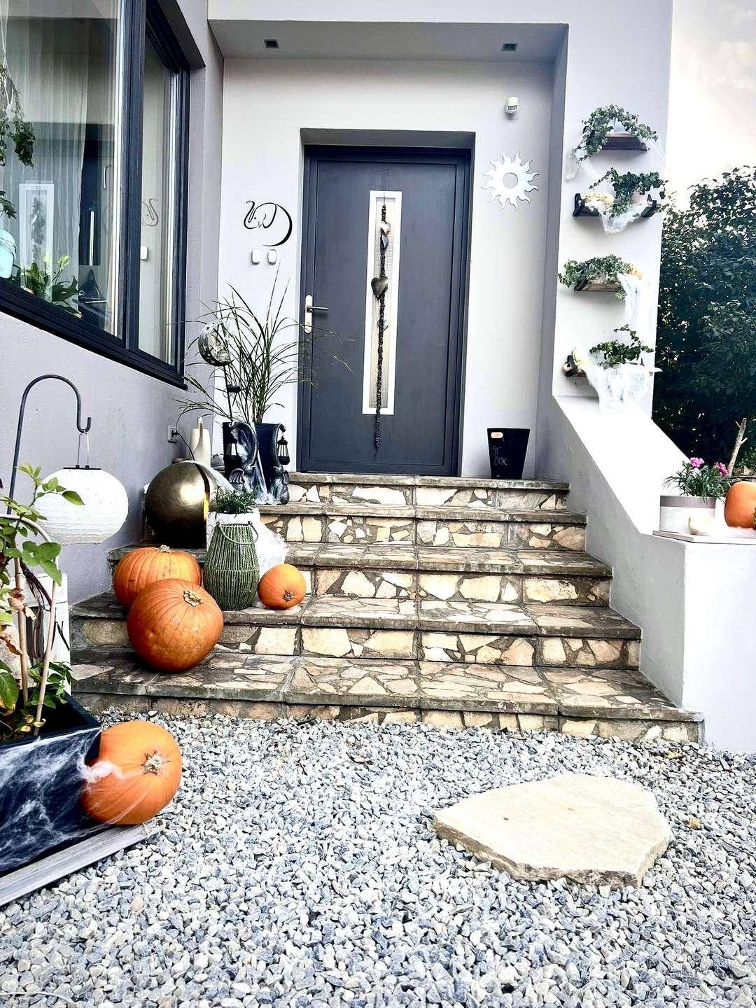 Eingangsbereich des Hauses mit Natursteintreppe, dunkler Haustür und herbstlicher Dekoration.