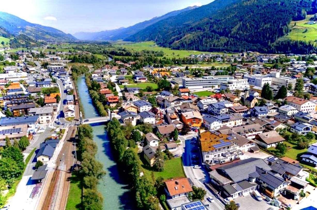 Luftaufnahme einer malerischen Stadt im Tal, durchzogen von einem Fluss und umgeben von Bergen.