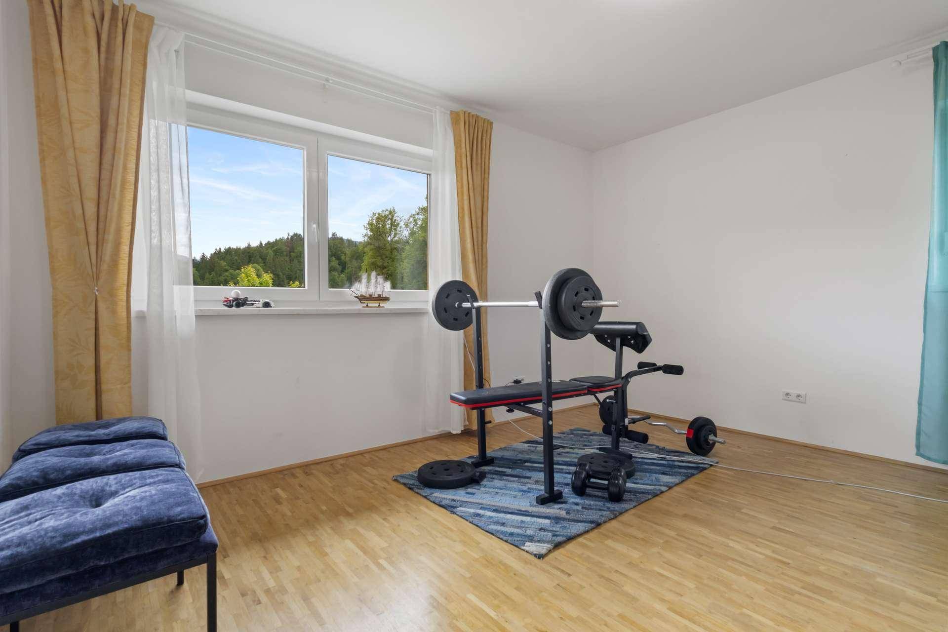 Fitnessraum mit Hantelbank und Gewichten, ideal für das Training zu Hause mit Blick ins Grüne.