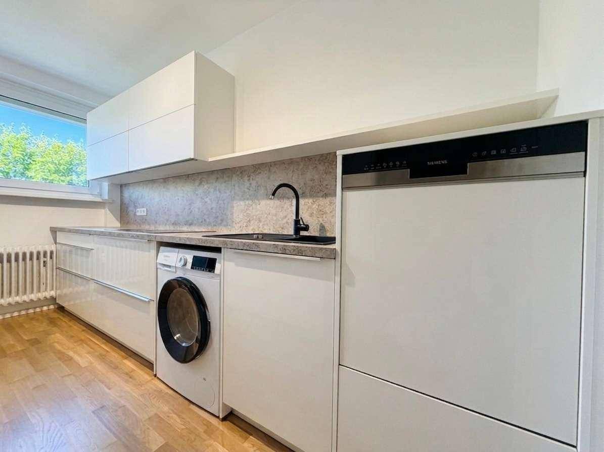 Moderne Küche mit weißen Hochglanzschränken, integrierter Waschmaschine und Geschirrspüler.