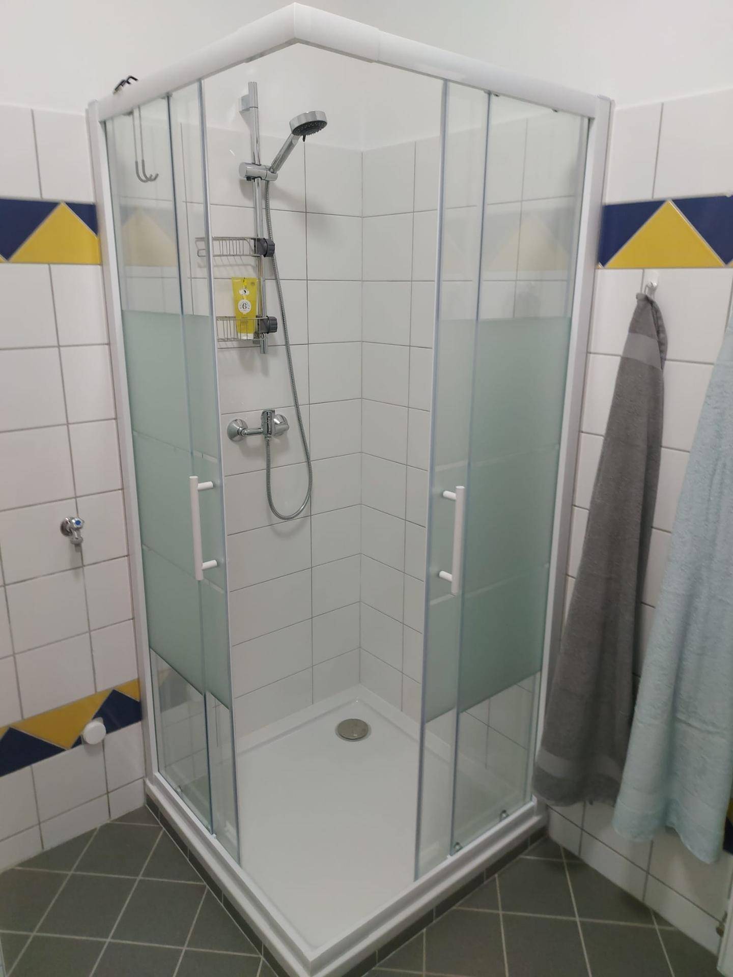 Eckduschkabine mit Glaswänden und Duscharmatur in einem gefliesten Badezimmer.