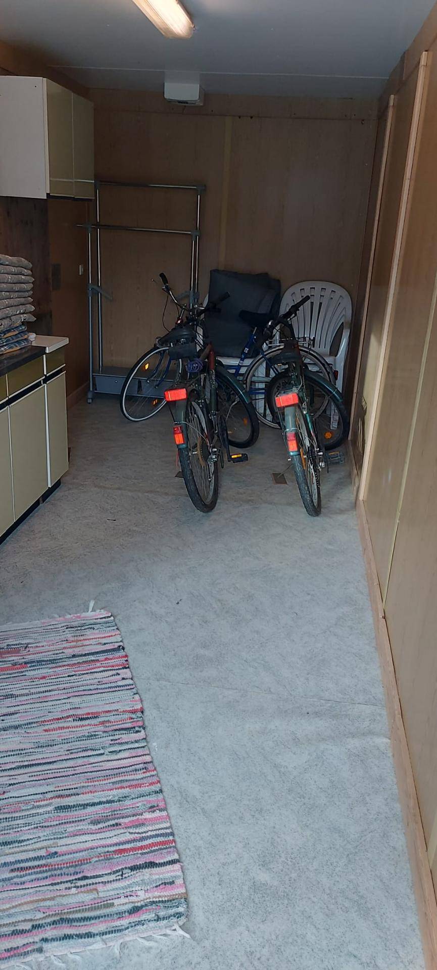 Funktionaler Abstellraum mit Fahrrädern, Schränken und einem gestreiften Teppich auf dem Boden.