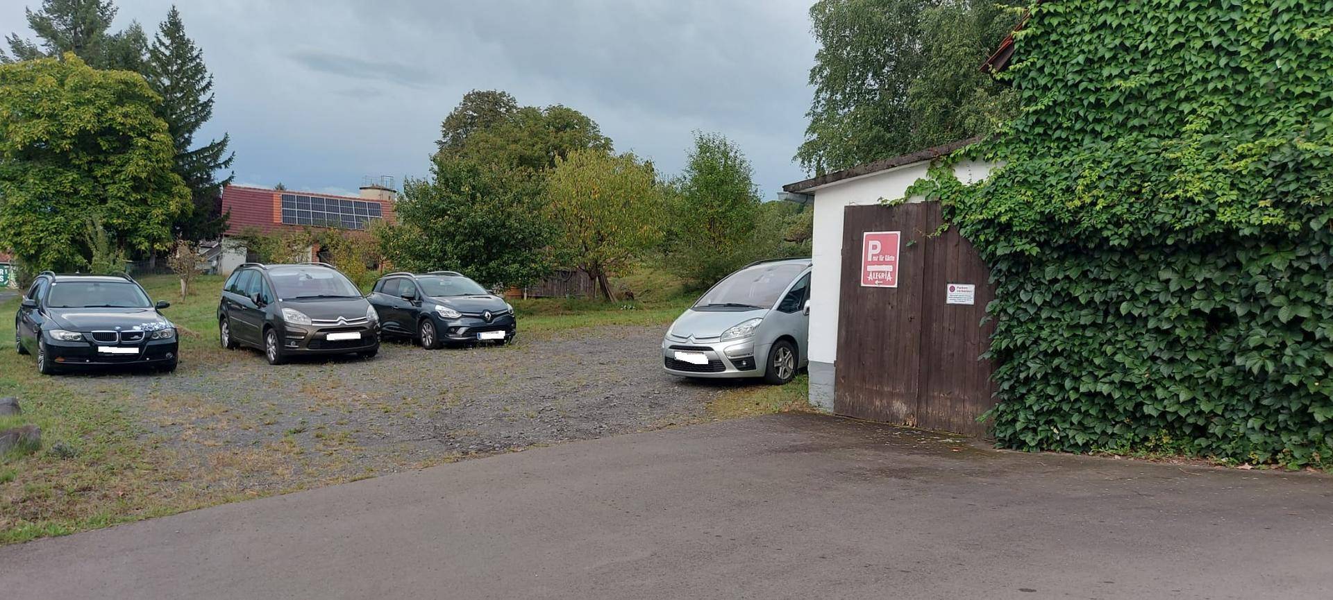 Außenbereich mit mehreren geparkten Autos und üppigem Grün, das ein Gebäude bedeckt.