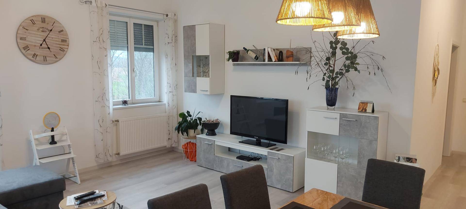 Moderner Wohnbereich mit TV-Möbeln, dekorativen Elementen und einem großen Fenster mit Blick ins Grüne.