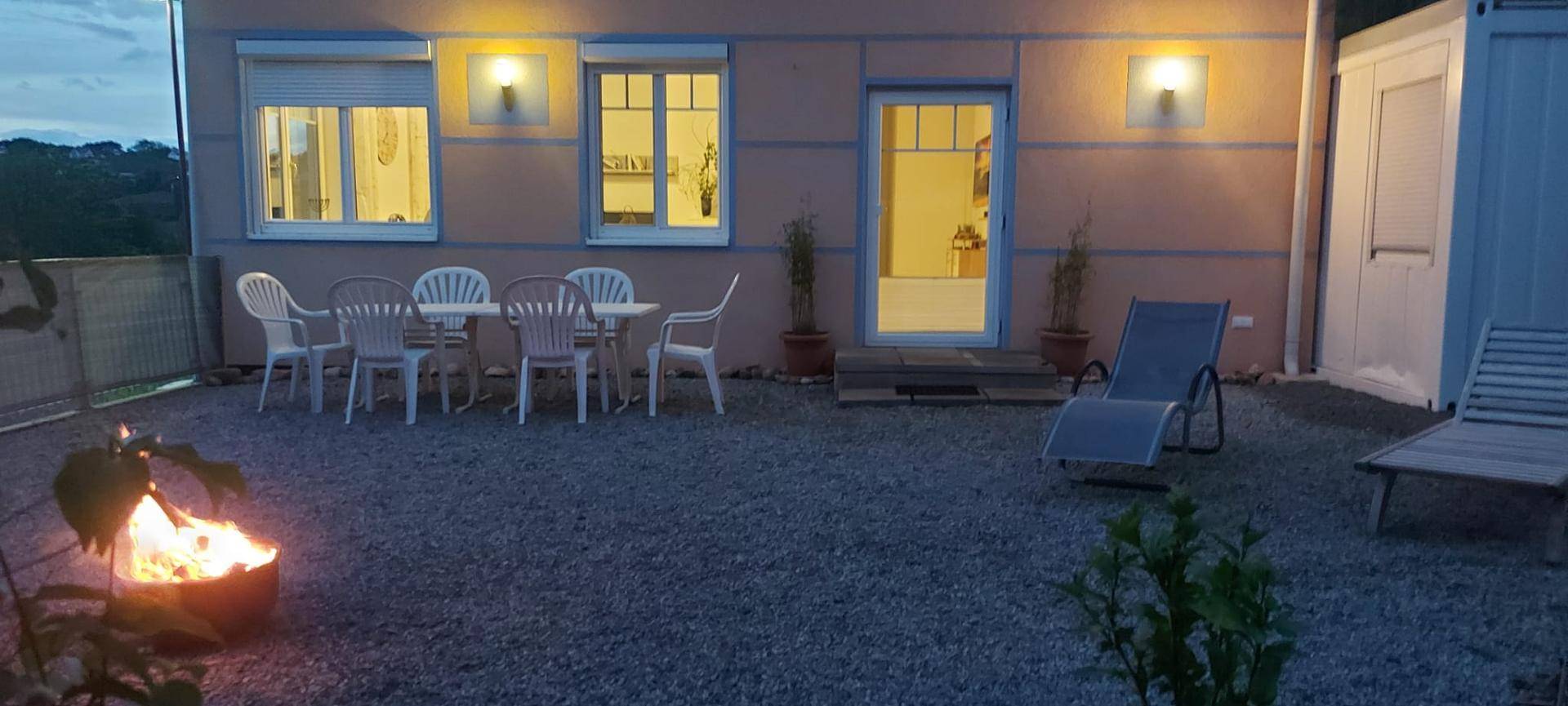 Gemütlicher Abend auf der Kiesterrasse mit beleuchtetem Sitzbereich und einer wärmenden Feuerschale.