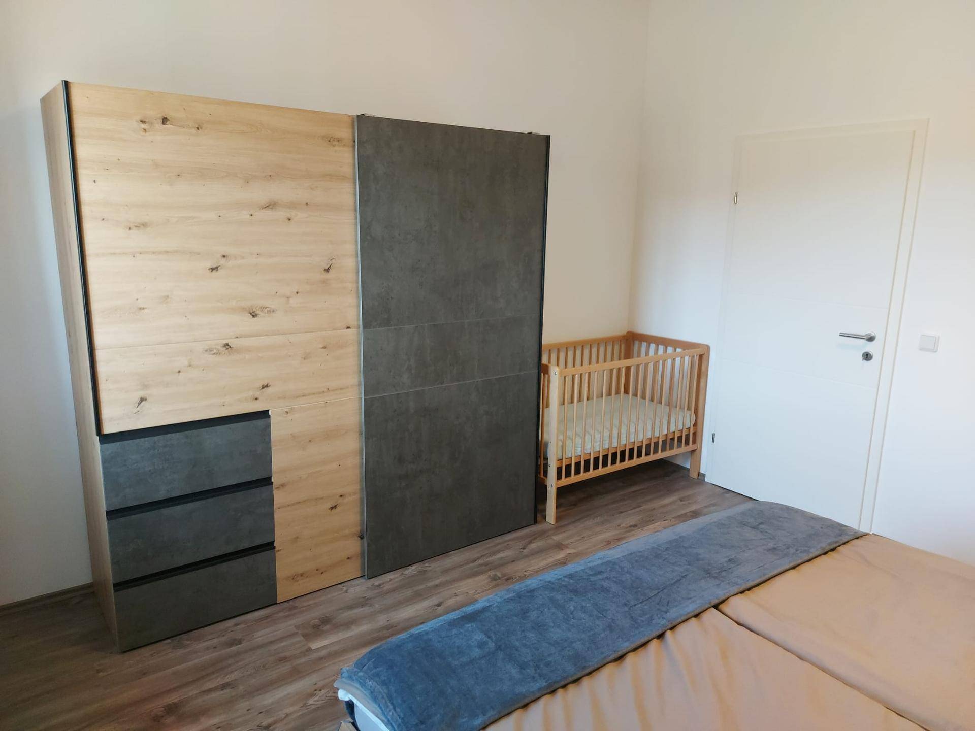 Schlafzimmer mit modernem Kleiderschrank, Babybett und hellem Laminatboden, ideal für eine Familie.