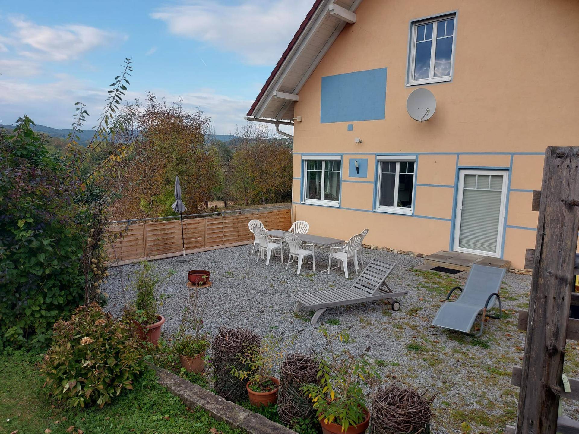 Hinterhofbereich mit Kiesfläche, Gartenmöbeln und Blick auf die grüne Umgebung, umgeben von einem Holzzaun.