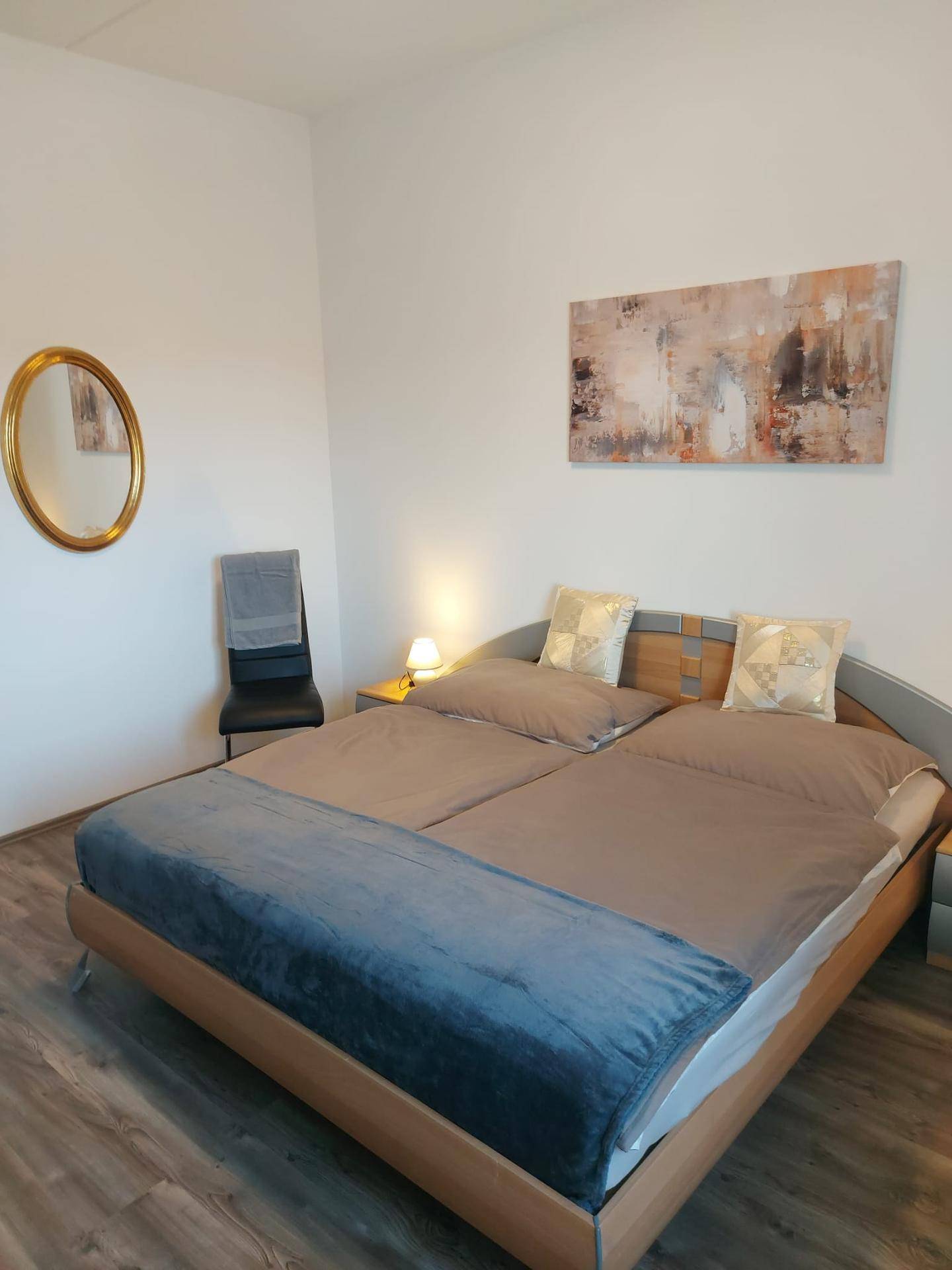 Gemütliches Schlafzimmer mit Doppelbett, Nachttischen und einem dekorativen Spiegel an der weißen Wand.