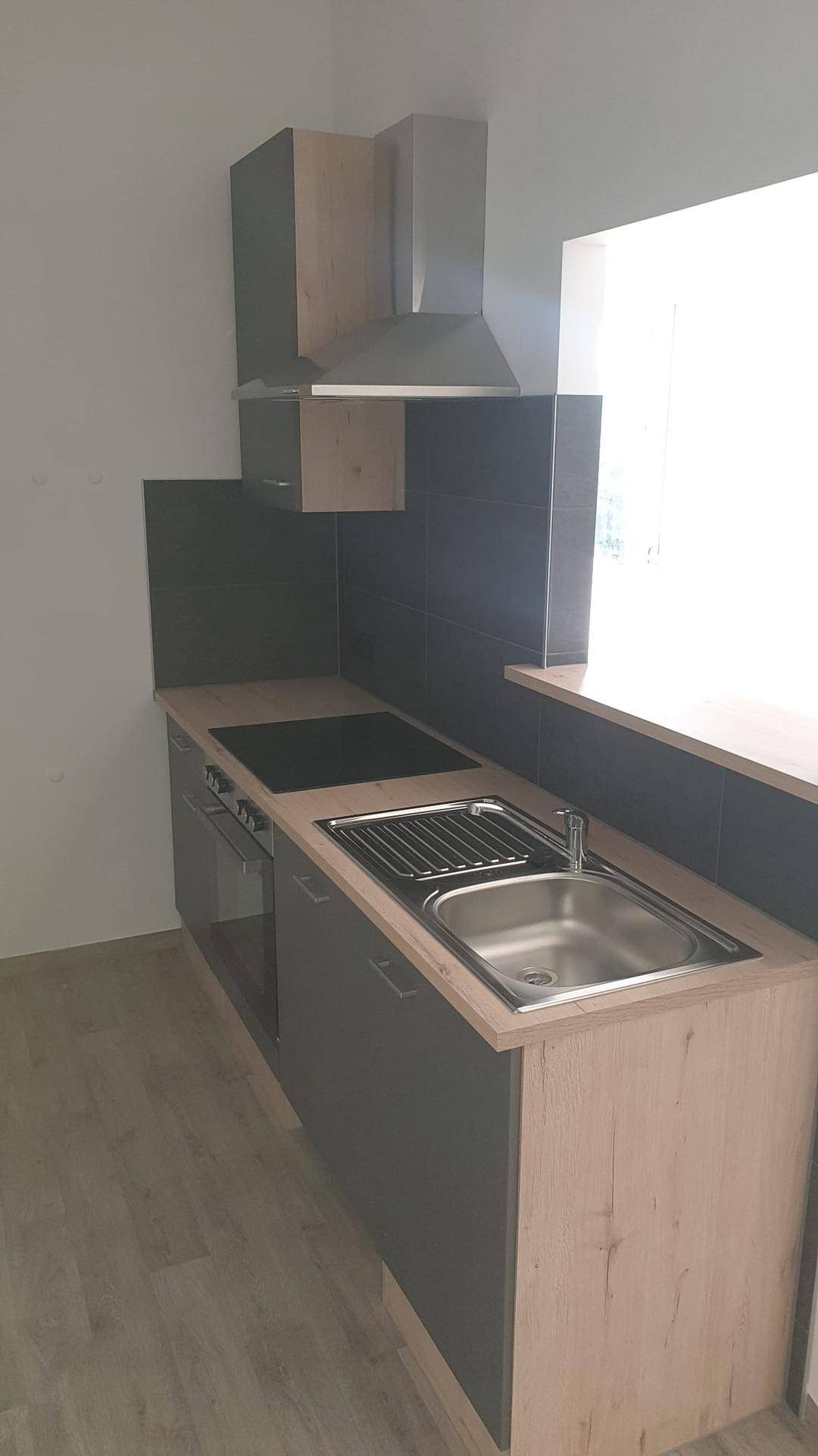 Kompakte Küchenzeile mit Spüle, Kochfeld und Dunstabzugshaube, ideal für kleine Wohnräume.