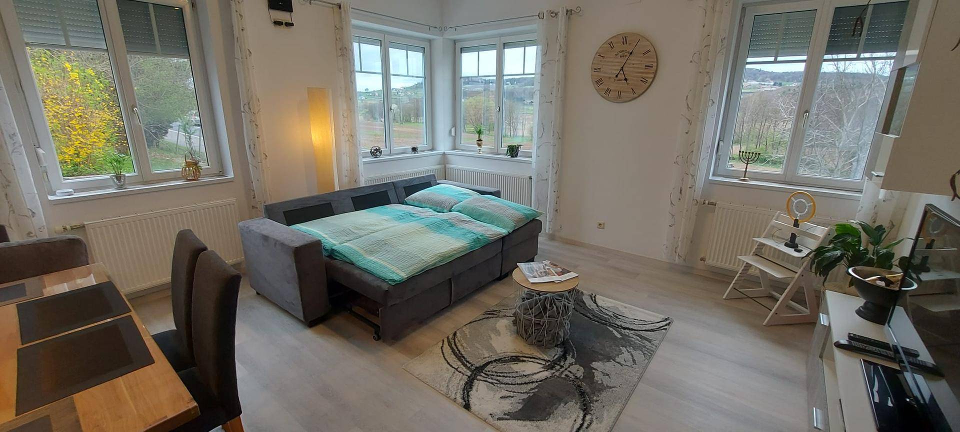 Geräumiger Wohnbereich mit ausgezogenem Schlafsofa, großen Fenstern und hellem Laminatboden.