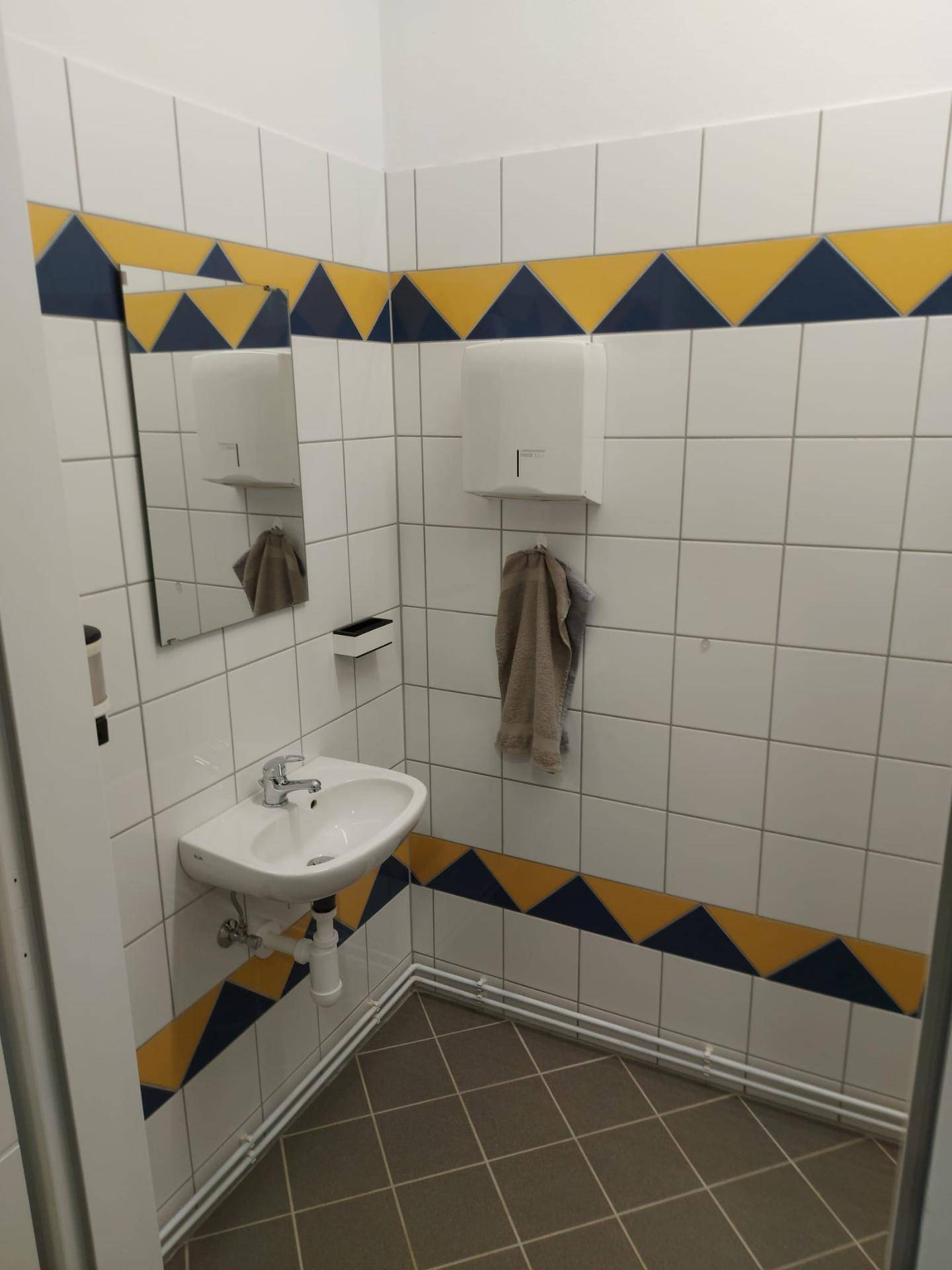 Kleines Gäste-WC mit Waschbecken und Spiegel, dekoriert mit gelb-blauen Fliesen.