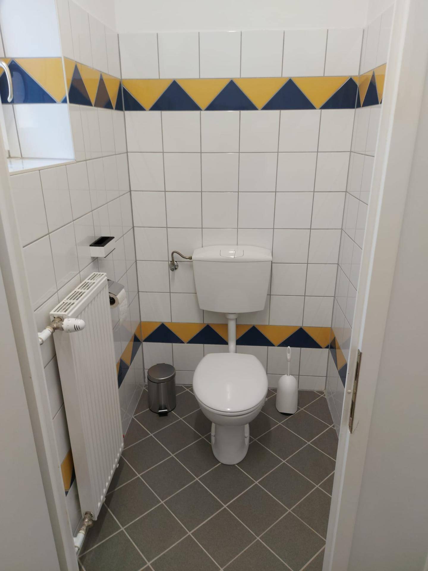 Kleines Gäste-WC mit weißen Wandfliesen und einem dekorativen blau-gelben Fliesenband.
