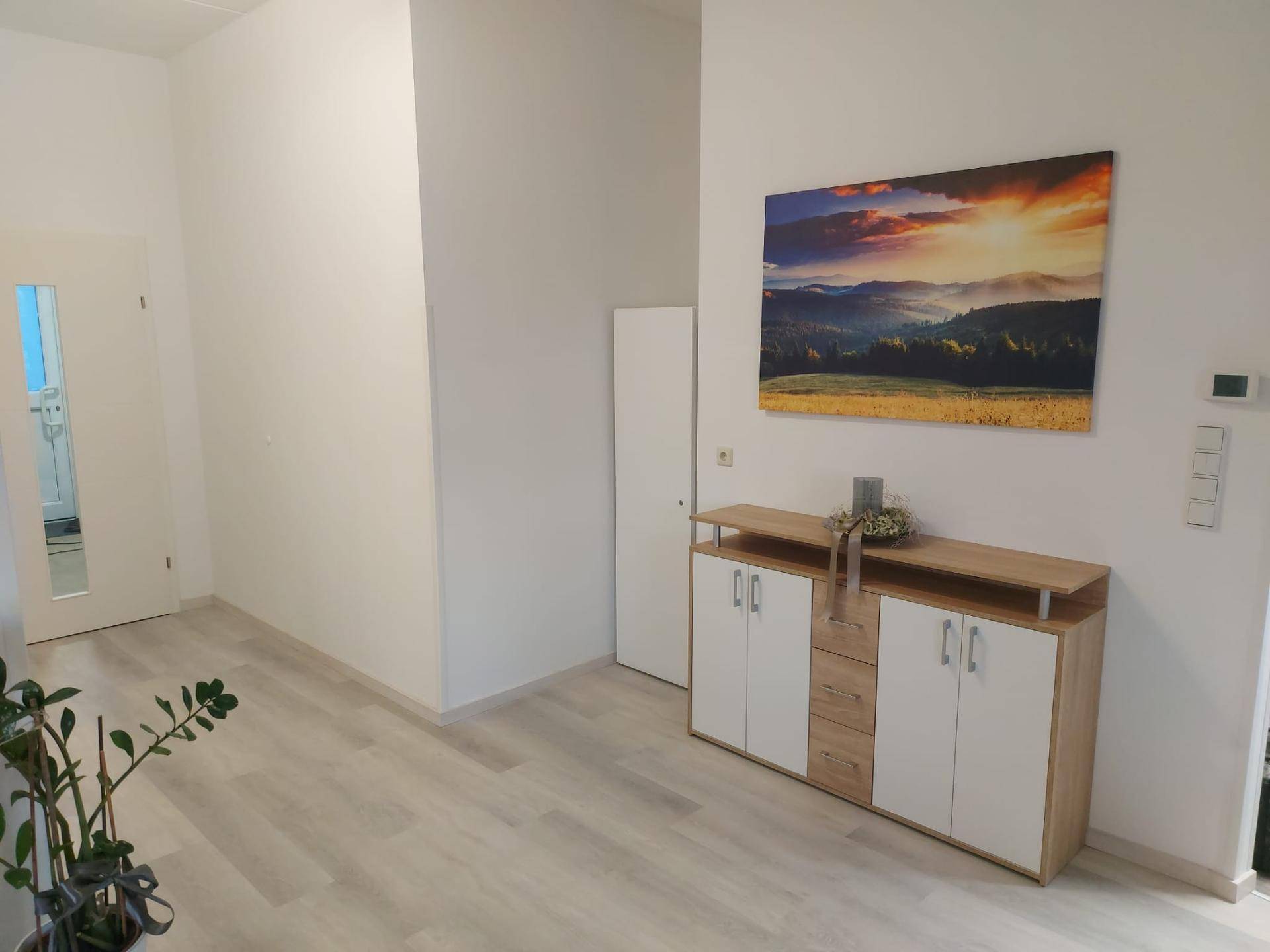 Heller Flur mit modernem Sideboard und einem großen Wandbild, das eine Landschaft zeigt.