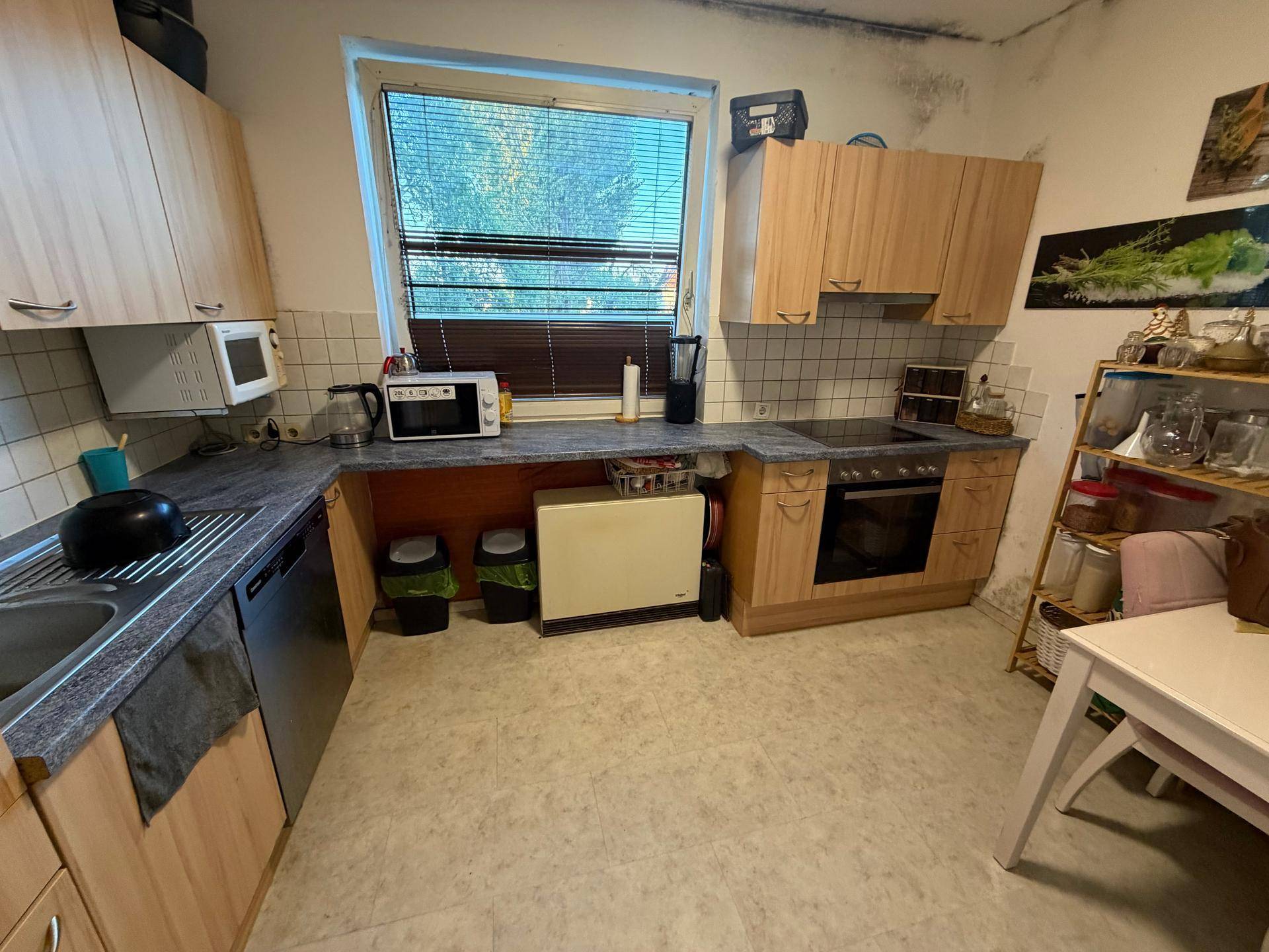 Funktionale Küche mit Holzschränken, Arbeitsplatte und Fenster mit Blick nach draußen.