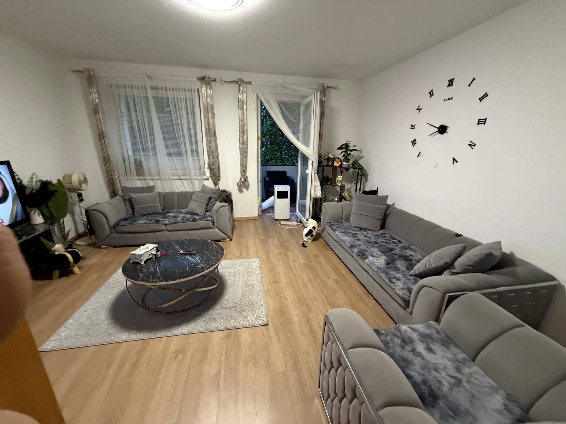 Geräumiges Wohnzimmer mit modernen Sofas, Holzboden und Zugang zu einem Balkon.
