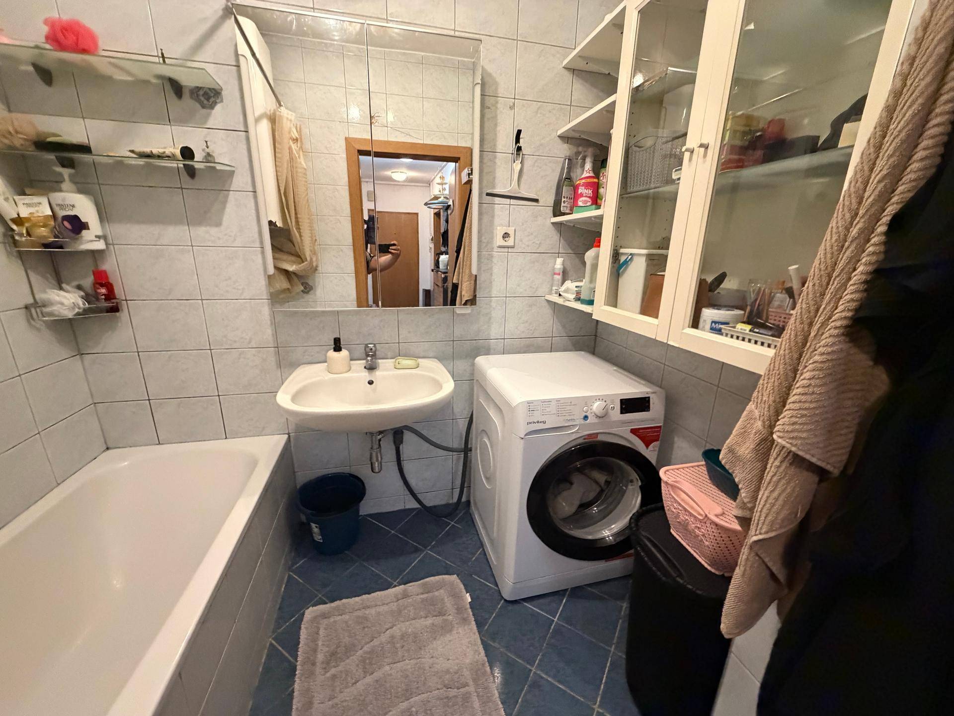 Gefliestes Badezimmer mit Badewanne, Waschbecken und integrierter Waschmaschine.