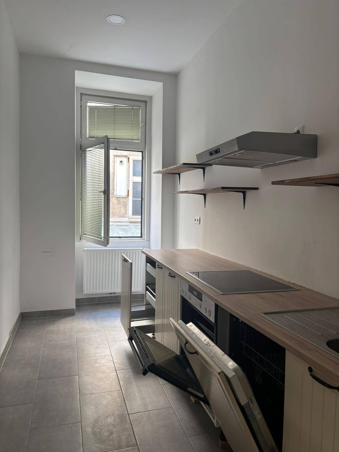 Moderne Küche mit grauen Fliesen, Fenster und einer Einbauküche mit Herd, Spüle und Dunstabzugshaube.