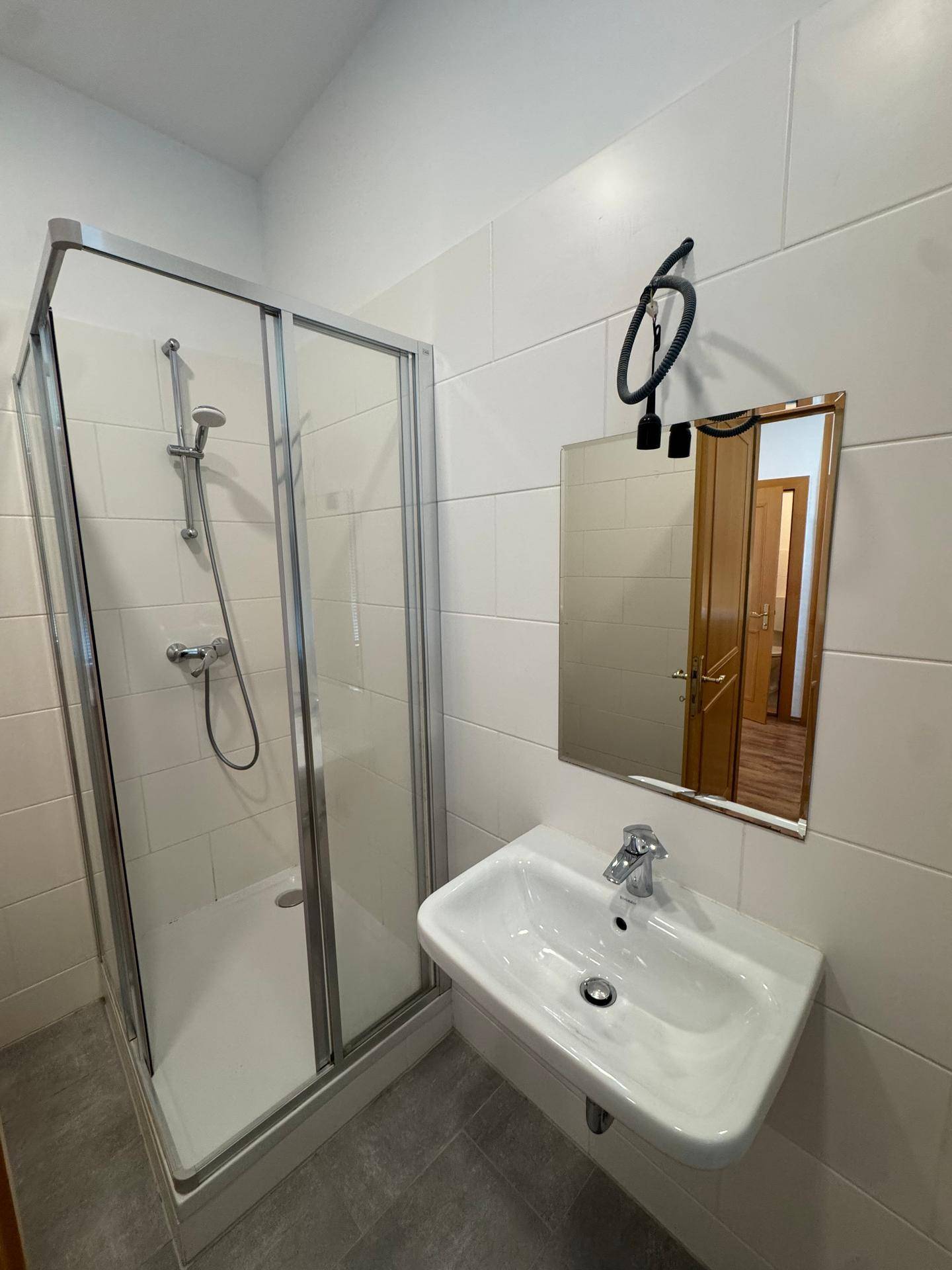 Modernes Badezimmer mit grauen Fliesen, weiß gefliesten Wänden, einer Duschkabine und einem Waschbecken.