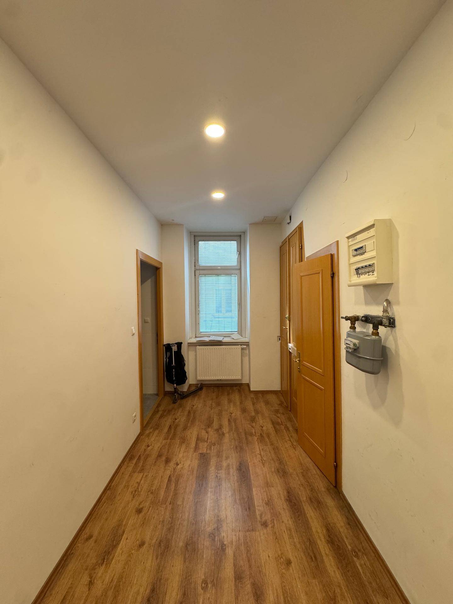 Heller Flur mit Laminatboden, einem Fenster am Ende und einem Sicherungskasten an der Wand.