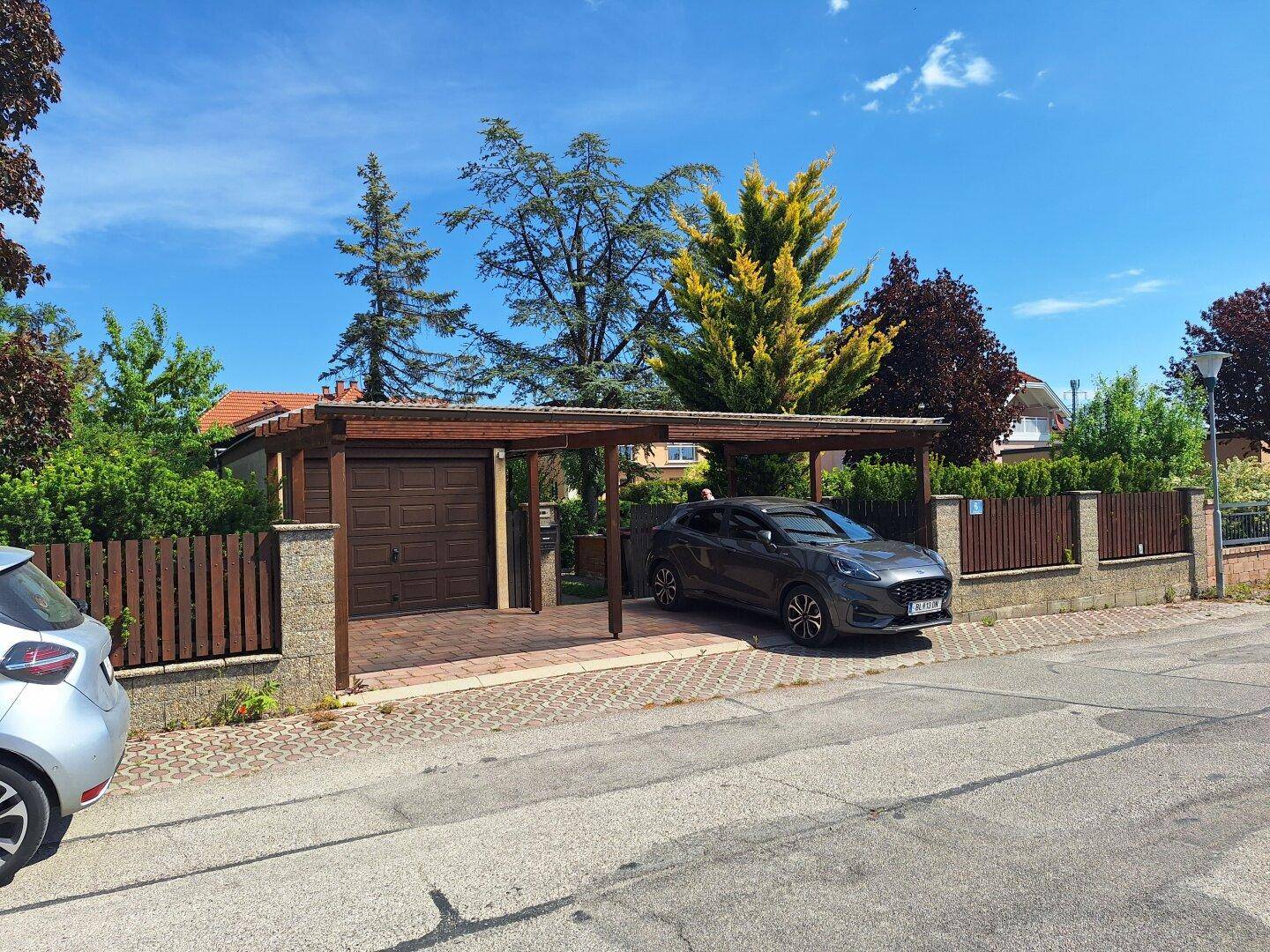 Carport und Garage mit Holzelementen bieten geschützten Parkraum vor dem Haus.