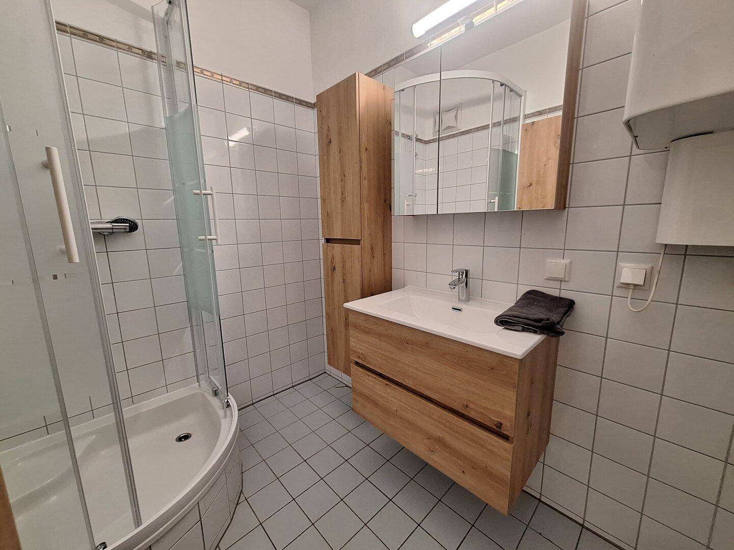Badezimmer mit Duschkabine, Holzwaschtisch und hellblauen Bodenfliesen.