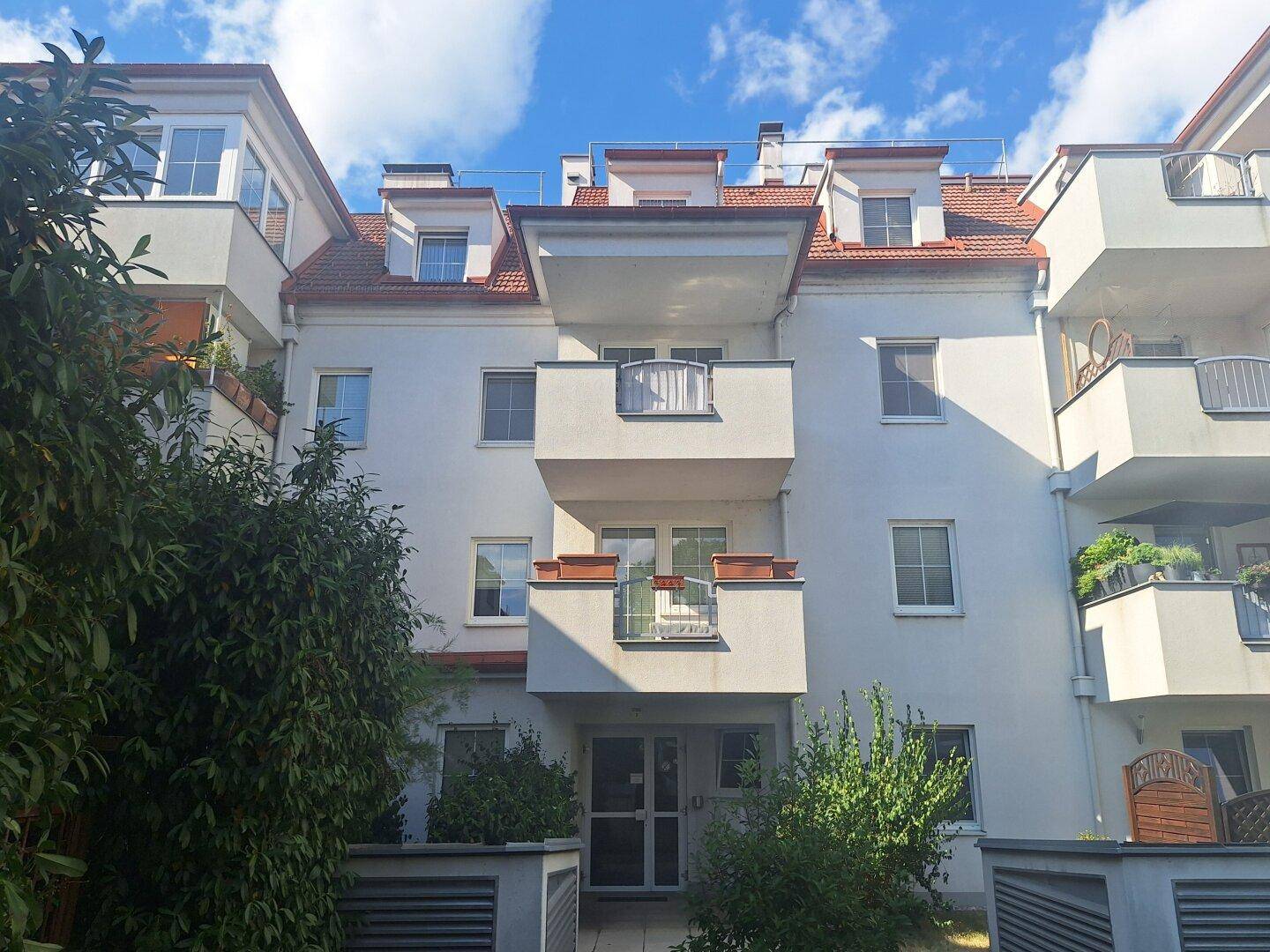 Fassade eines Wohngebäudes mit mehreren Balkonen und Fenstern unter blauem Himmel.