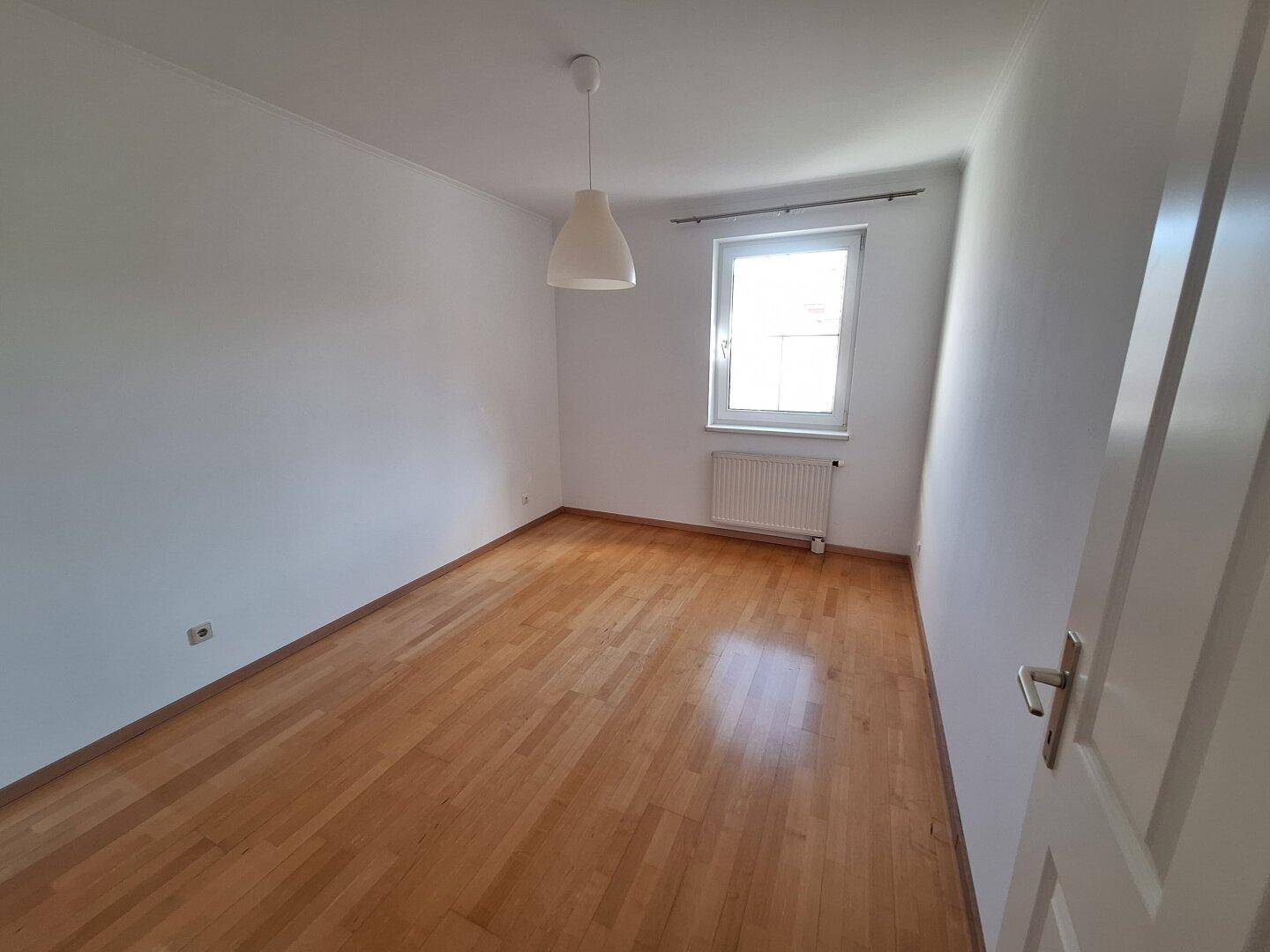Helles Schlafzimmer mit Parkettboden, weißen Wänden und einem Fenster für Tageslicht.