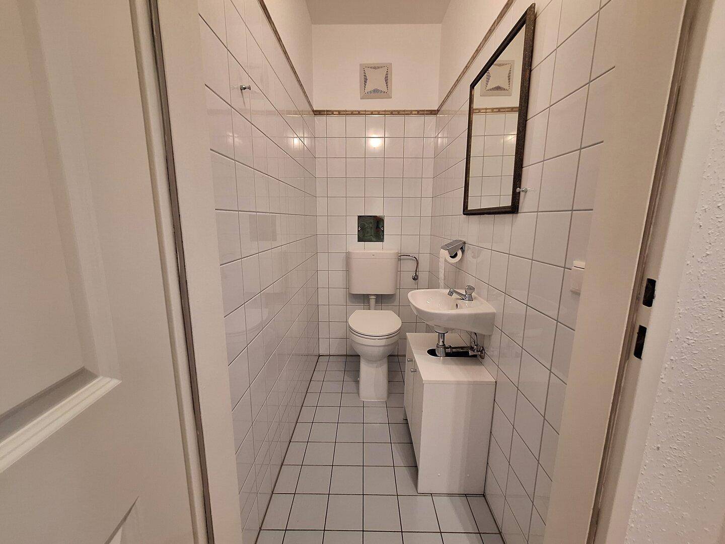 Kleines Gäste-WC mit weißen Fliesen, Toilette und Handwaschbecken.