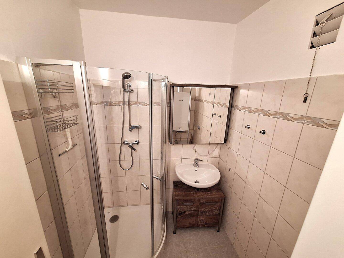 Badezimmer mit Eckdusche, Einzelwaschbecken und hellen Fliesen an den Wänden.