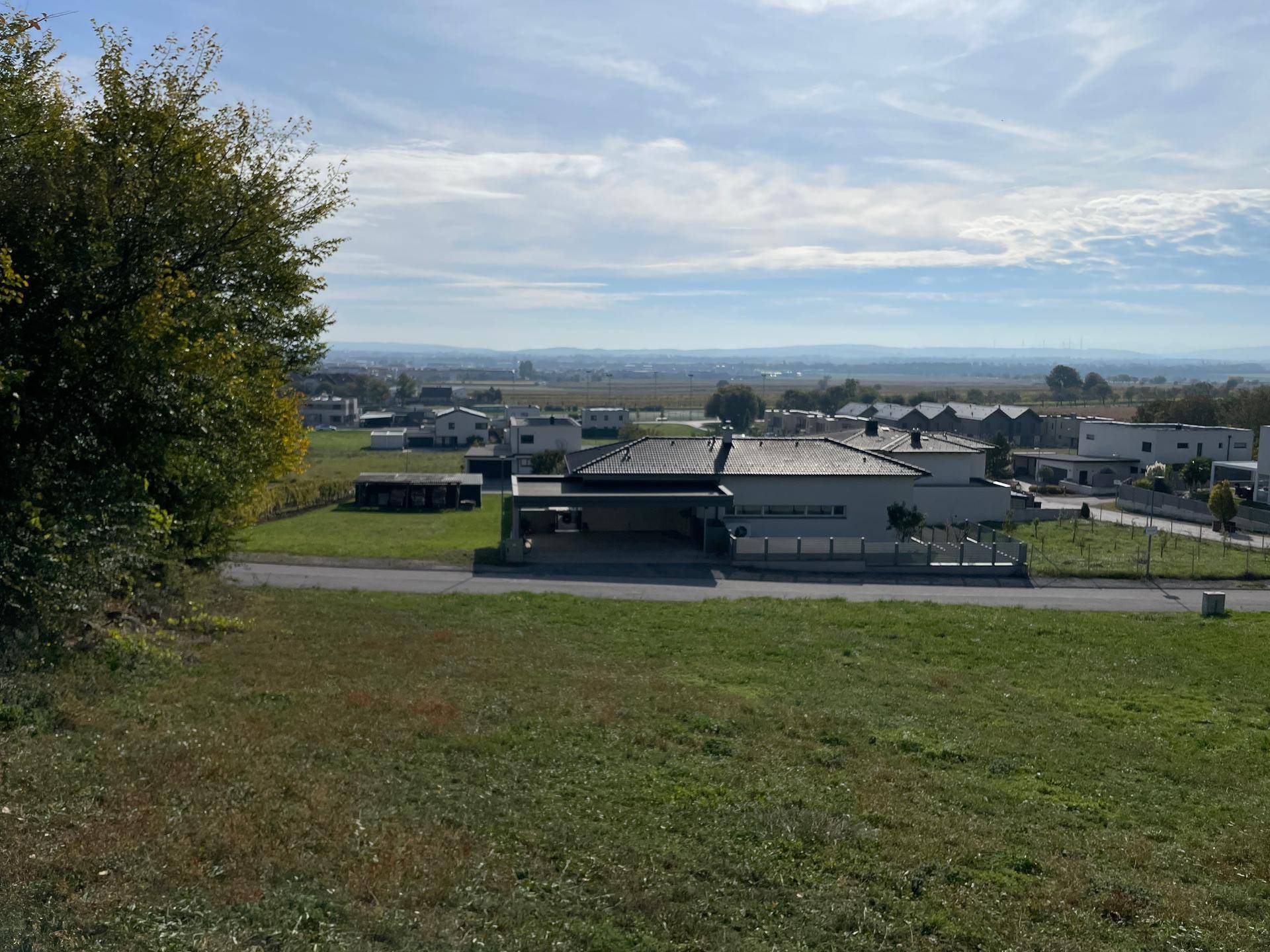 Panoramablick von einem erhöhten Grundstück auf eine ländliche Wohnsiedlung und weite Landschaft.