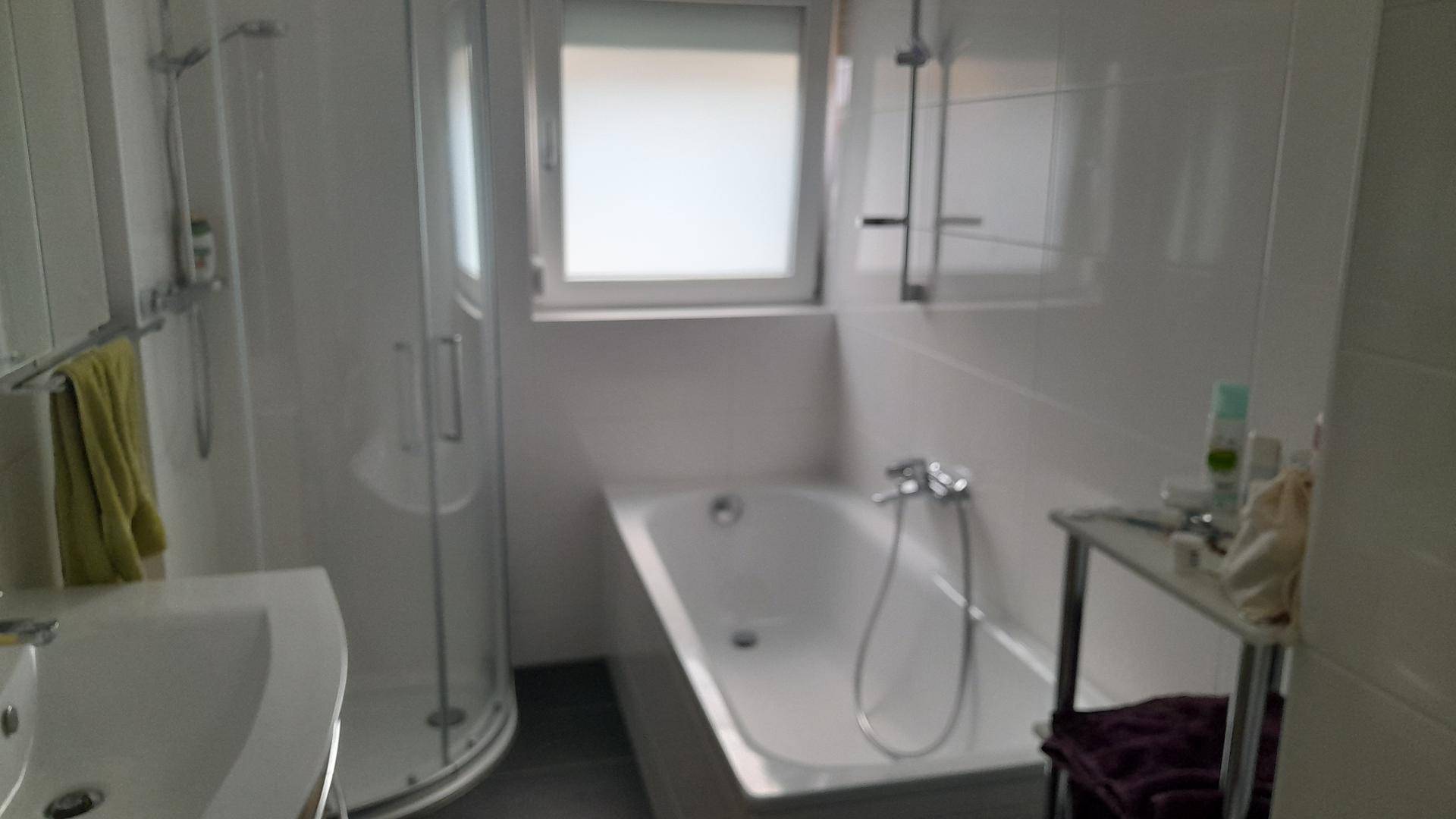 Helles Badezimmer mit Badewanne, Duschkabine, Waschbecken und Fenster.