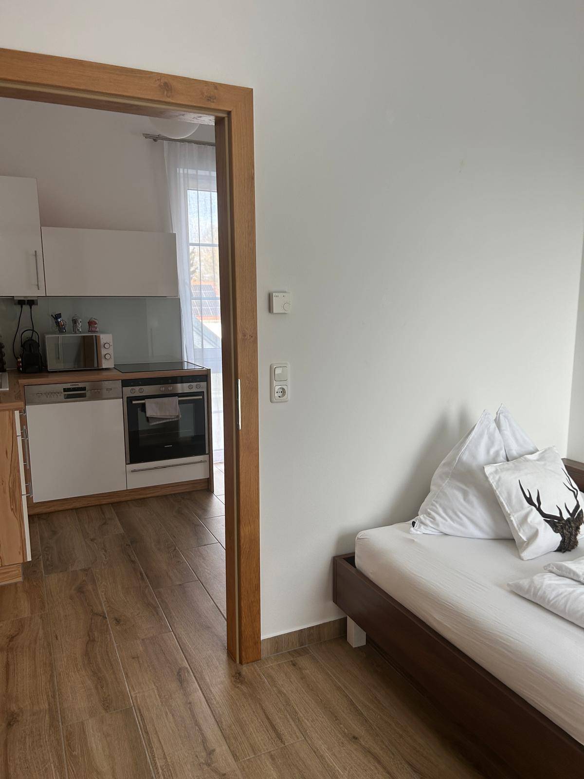 Schlafzimmer mit Holzboden und Blick durch die Tür in eine angrenzende moderne Küche.