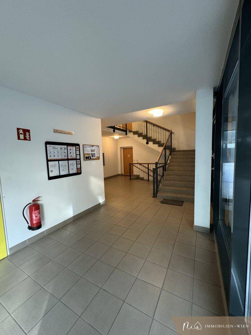 Geräumiger Eingangsbereich mit Fliesenboden, Treppenhaus und Brandschutzvorrichtungen.