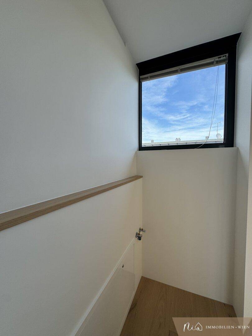 Treppenhaus mit Holzgeländer, Fenster und Parkettboden, führt zu den oberen Etagen.